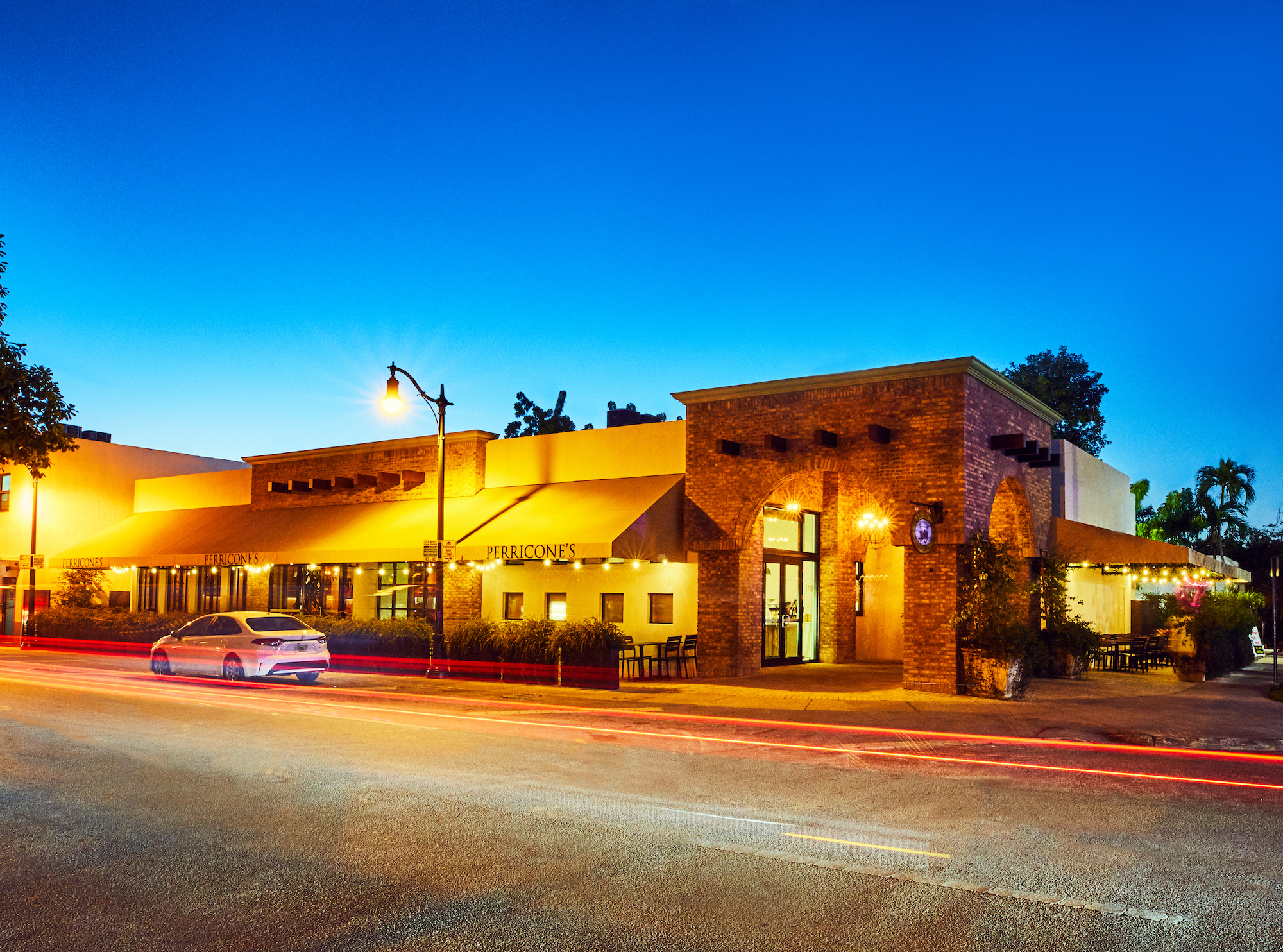 Exterior of Perricone's at dusk. car and tail light trails visible in foreground