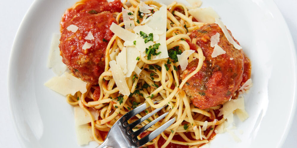 Fork digging into a plate of spaghetti and meatballs
